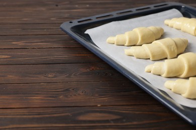 Photo of Fresh raw croissants on wooden table, closeup. Space for text