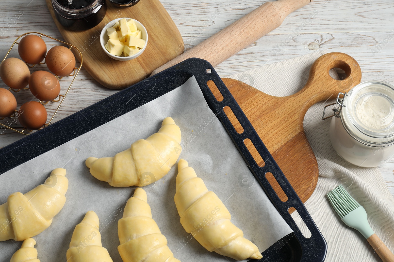 Photo of Raw croissants, ingredients and kitchenware on wooden table, flat lay