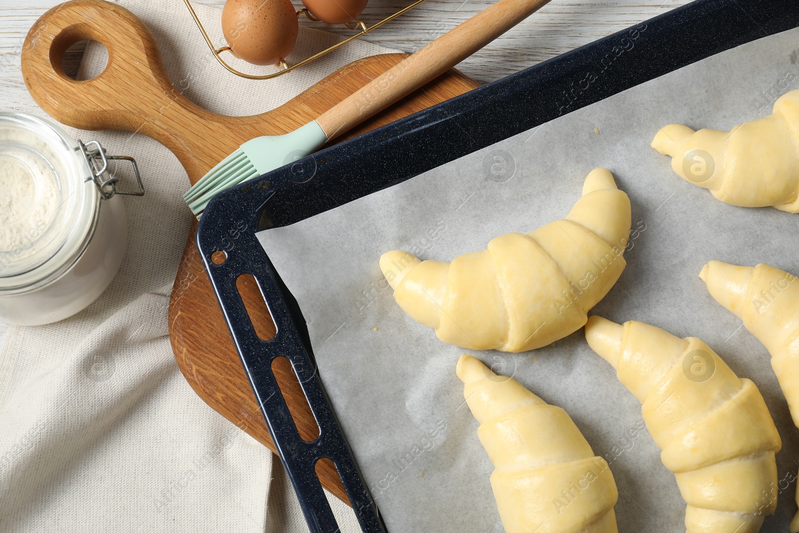 Photo of Raw croissants, brush, flour and eggs on wooden table, flat lay