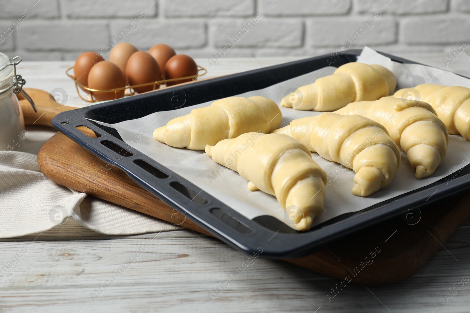 Photo of Raw croissants and eggs on wooden table against brick wall, closeup