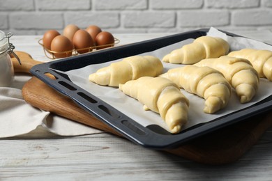 Raw croissants and eggs on wooden table against brick wall, closeup