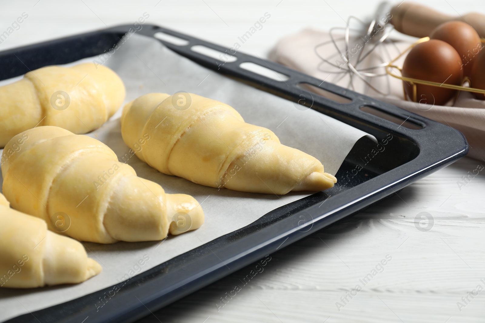 Photo of Raw croissants and eggs on white wooden table, closeup