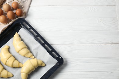 Raw croissants and eggs on white wooden table, flat lay. Space for text