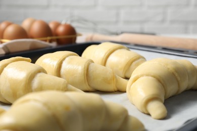 Photo of Raw croissants on table against white brick wall, closeup