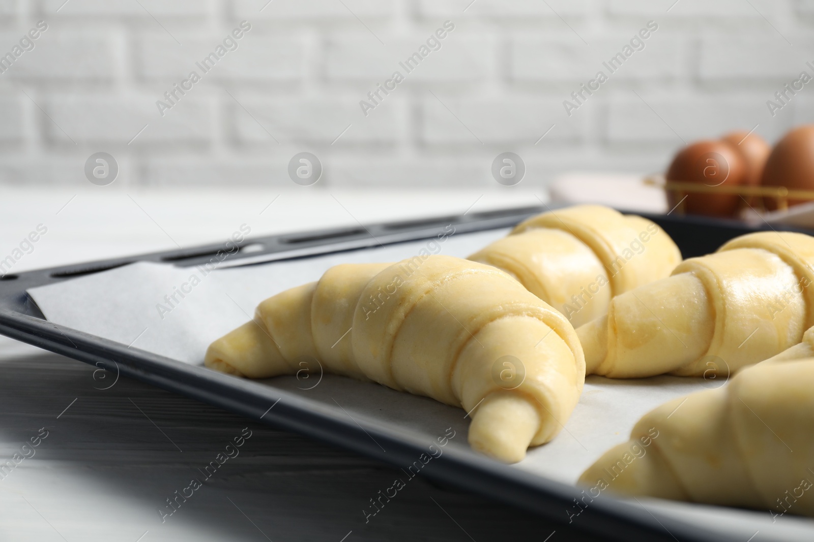 Photo of Raw croissants on white wooden table against brick wall, closeup