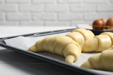 Raw croissants on white wooden table against brick wall, closeup