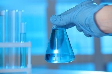 Photo of Woman holding flask with blue liquid indoors, closeup