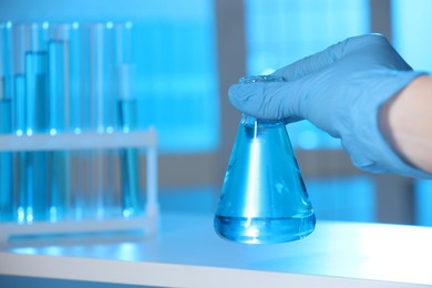 Photo of Woman holding flask with blue liquid indoors, closeup