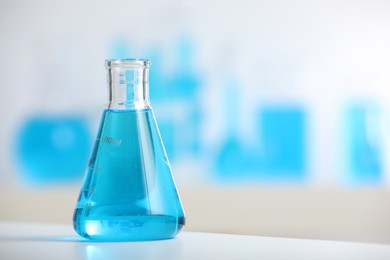 Photo of Conical flask with blue liquid on table indoors, closeup. Space for text