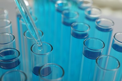 Photo of Dripping liquid into test tubes on light background, closeup