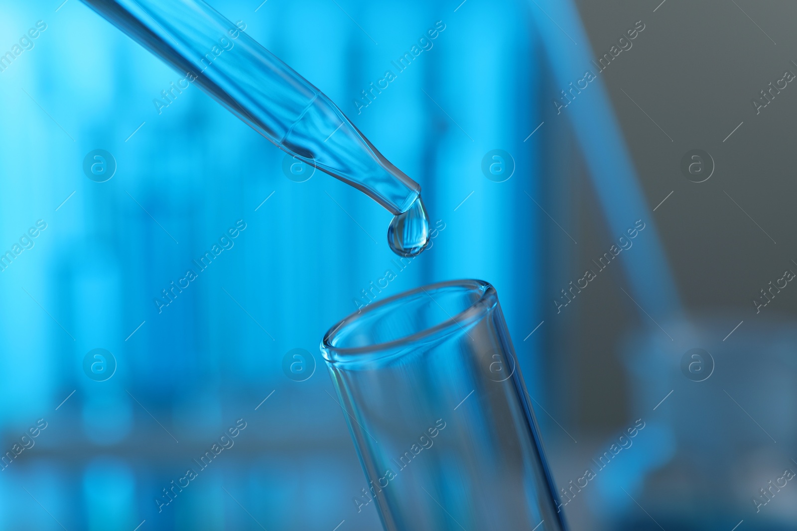 Photo of Dripping liquid into test tube on blurred background, closeup