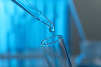 Photo of Dripping liquid into test tube on blurred background, closeup