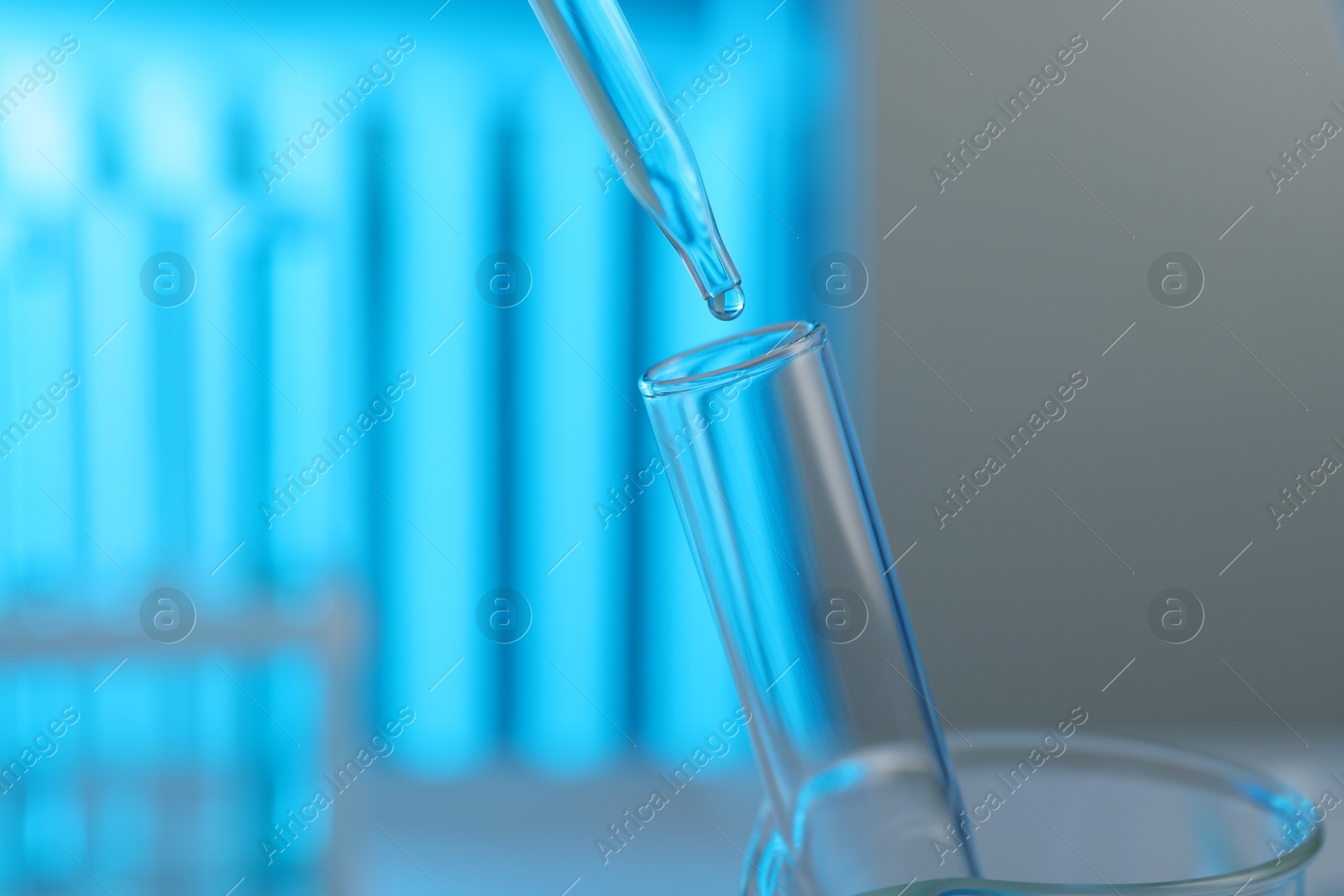 Photo of Dripping liquid into test tube on blurred background, closeup