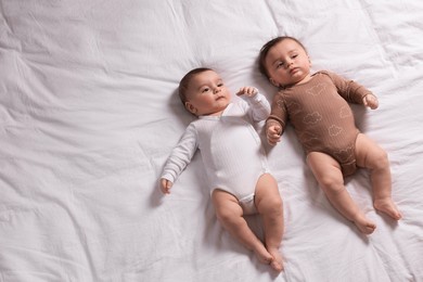 Photo of Cute twin babies resting on bed indoors, top view. Space for text