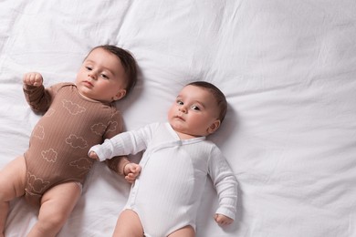 Photo of Cute twin babies resting on bed indoors, top view. Space for text