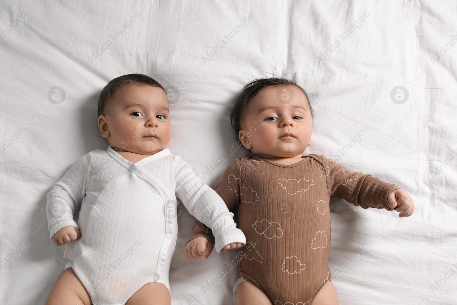 Photo of Cute twin babies resting on bed indoors, top view