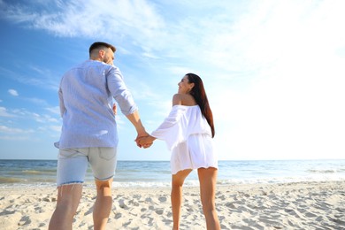 Photo of Lovely couple running together on beach, back view