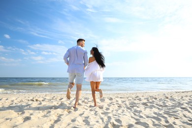 Photo of Lovely couple running together on beach, back view