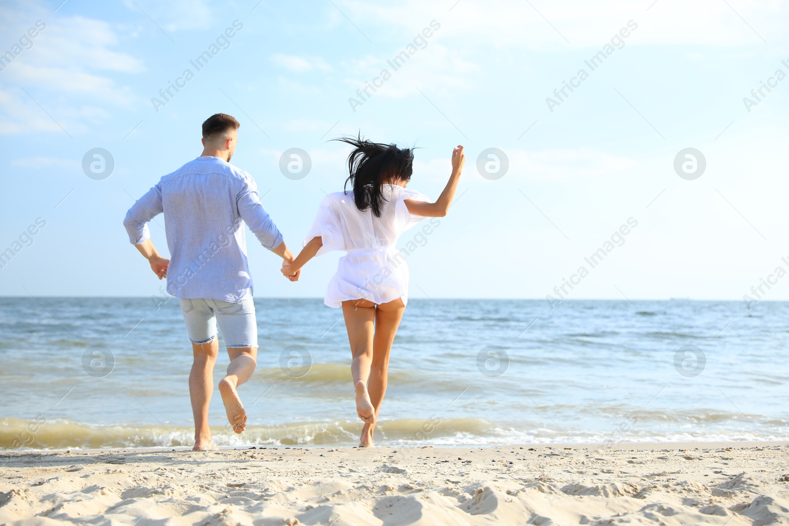 Photo of Lovely couple running together on beach, back view