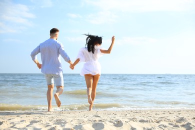 Photo of Lovely couple running together on beach, back view