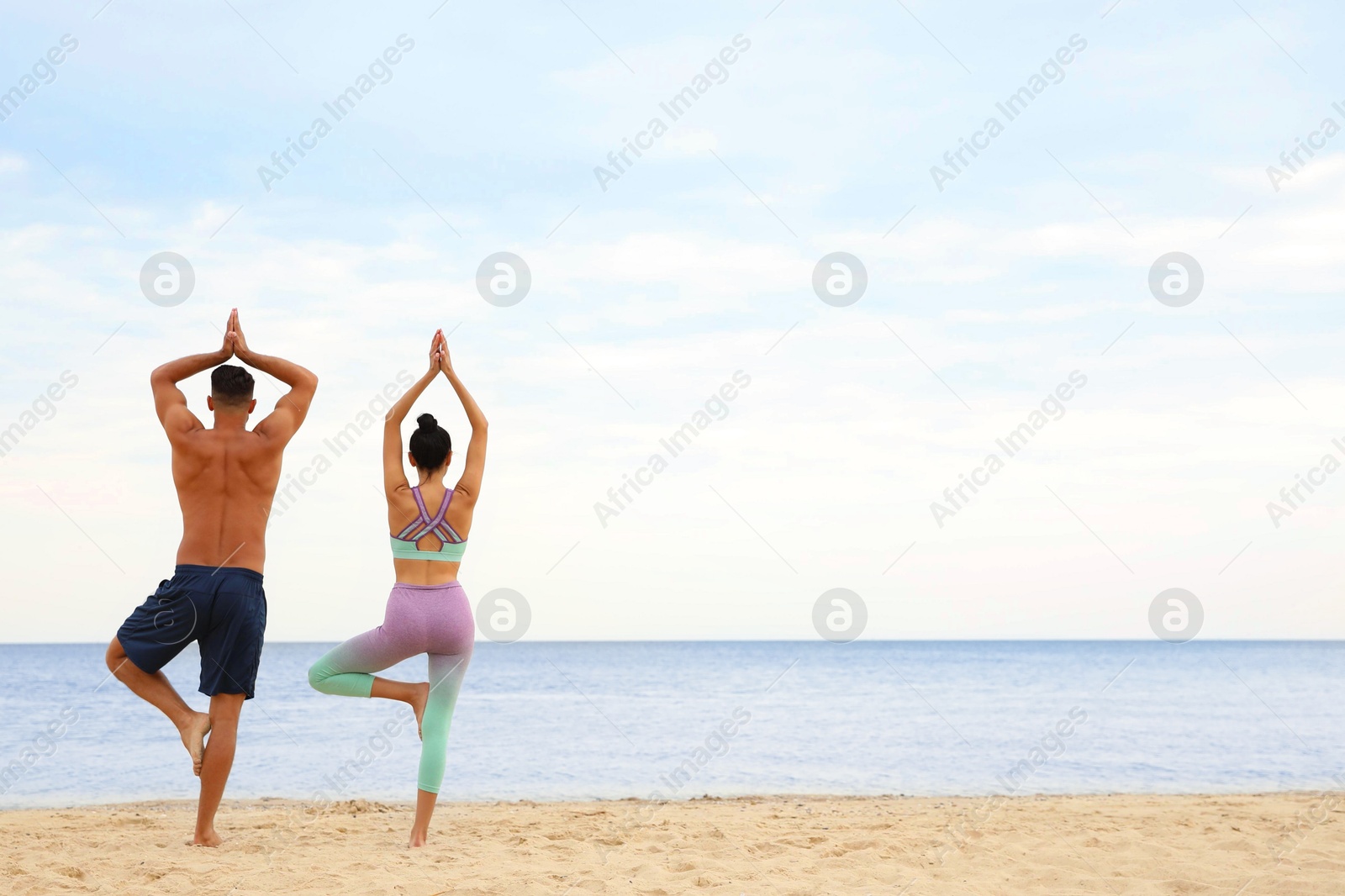 Photo of Couple practicing yoga on beach, back view with space for text. Body training