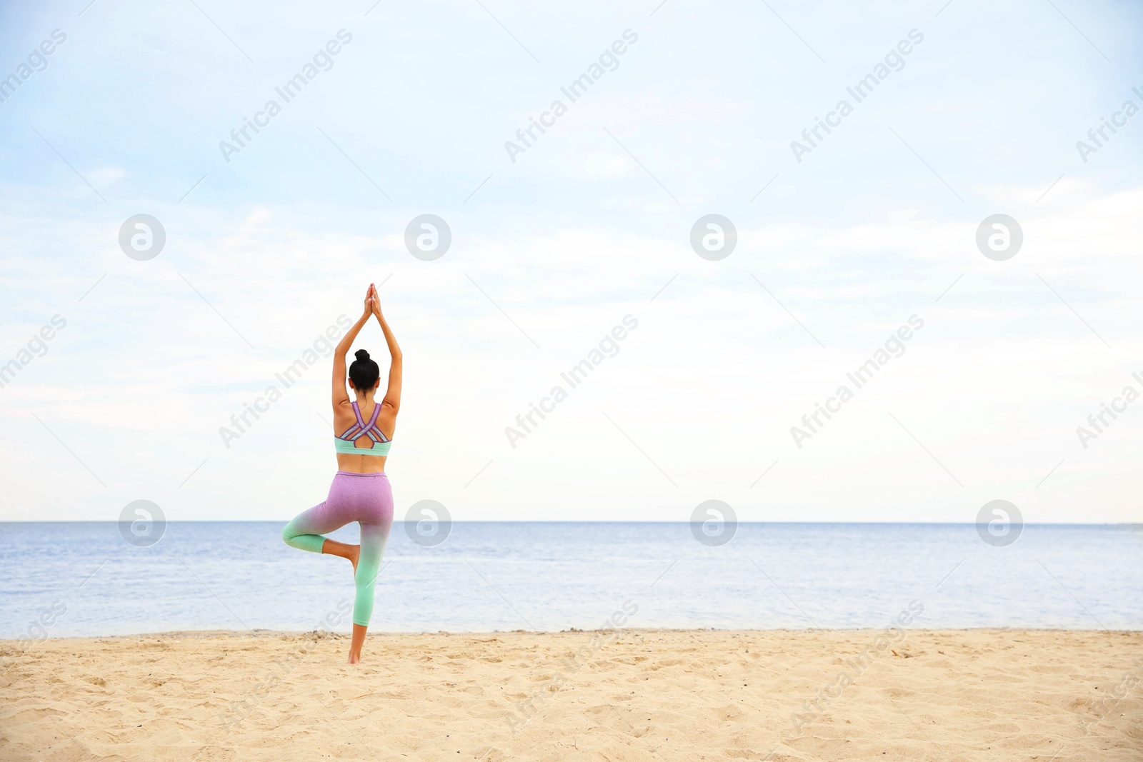 Photo of Young woman practicing yoga on beach, back view with space for text. Body training