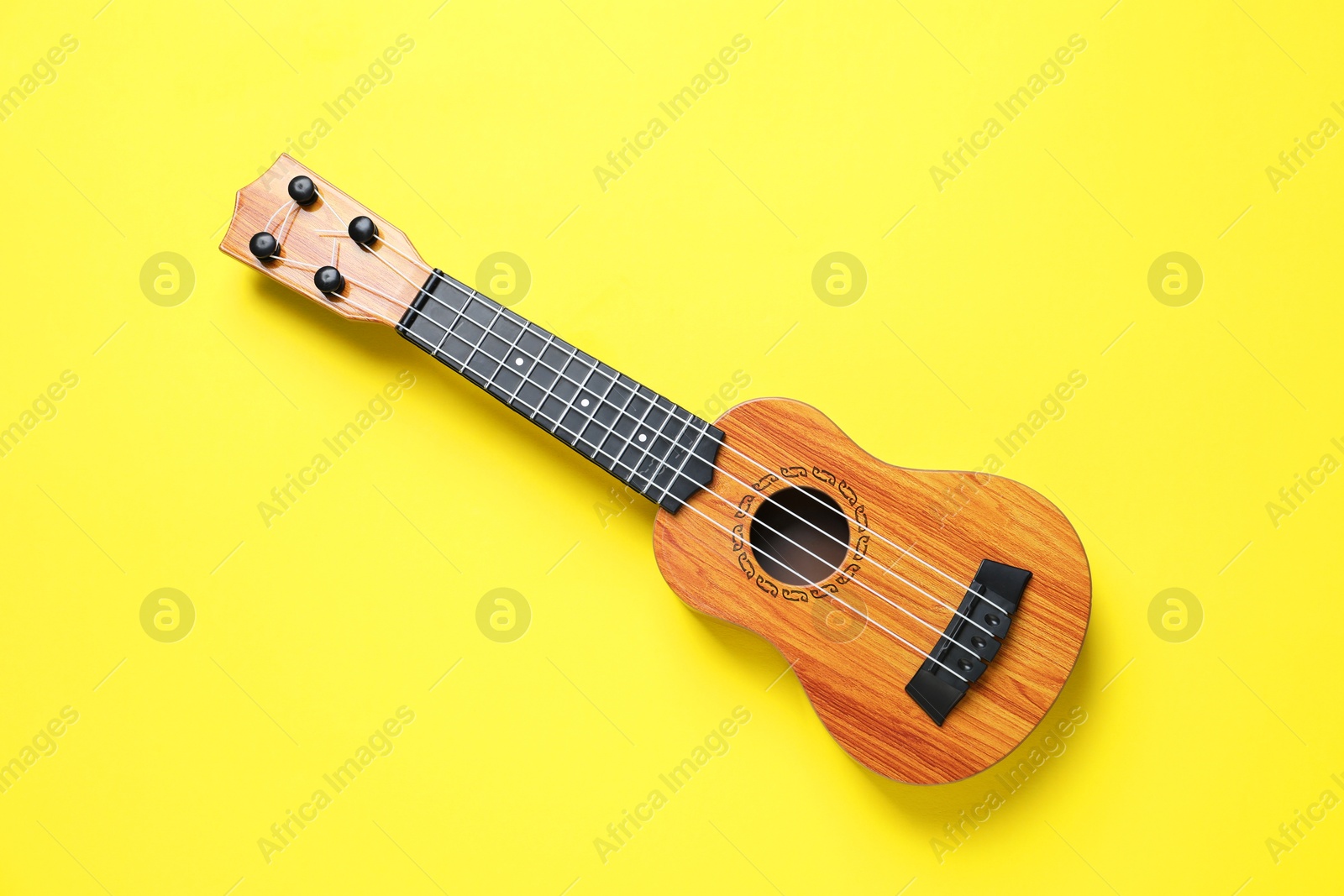 Photo of One ukulele on yellow background, top view