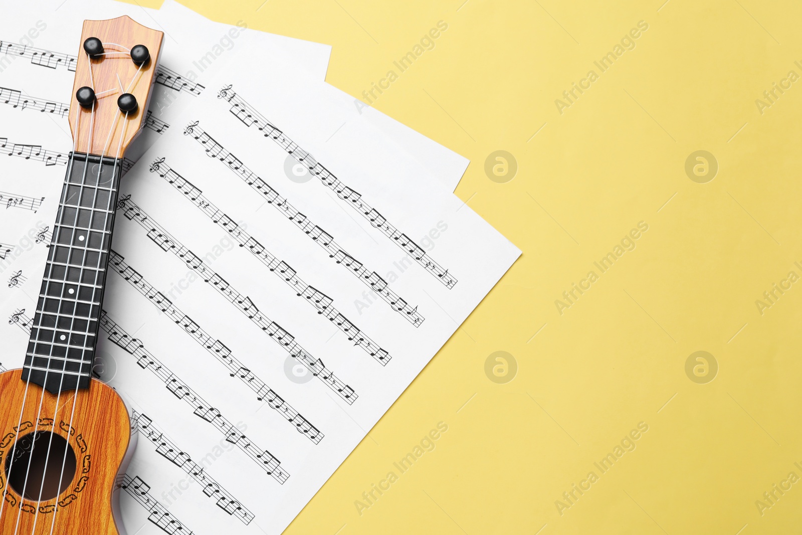 Photo of Ukulele and music sheets on yellow background, top view. Space for text