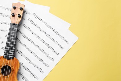 Photo of Ukulele and music sheets on yellow background, top view. Space for text