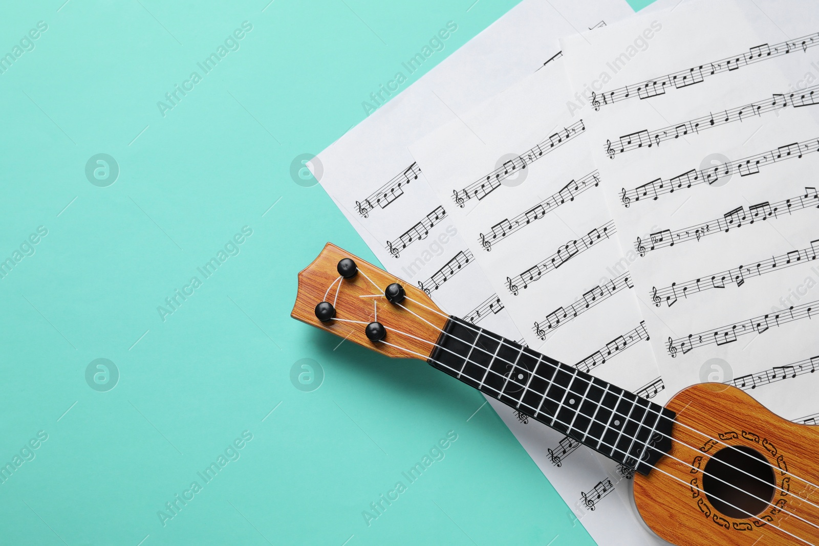 Photo of Ukulele and music sheets on turquoise background, top view. Space for text