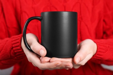 Photo of Woman holding blank black ceramic mug, closeup. Mockup for design