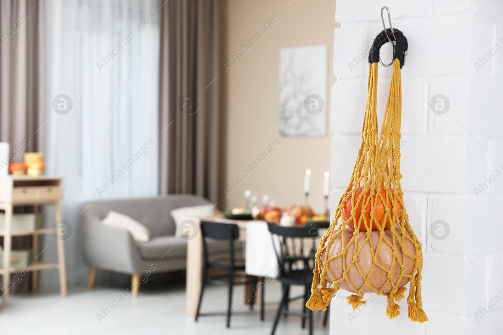 Photo of Macrame bag with products hanging on white brick wall indoors