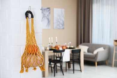 Photo of Macrame bag with products hanging on white brick wall indoors