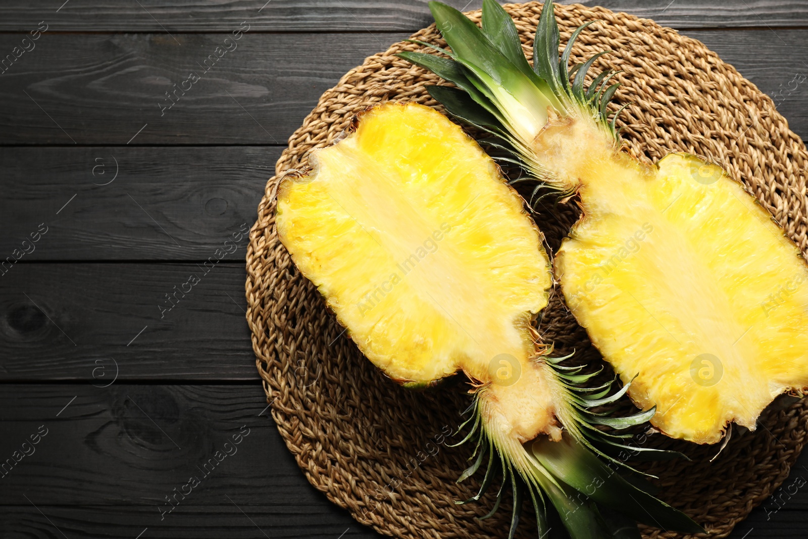 Photo of Halves of ripe pineapple on black wooden table, top view. Space for text