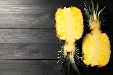 Halves of ripe pineapple on black wooden table, top view. Space for text