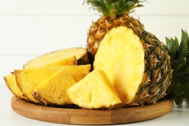 Photo of Whole and sliced fresh ripe pineapples on white table, closeup