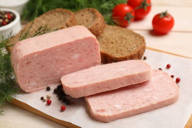 Pieces of tasty canned meat, peppercorns, dill and bread on light wooden table, closeup