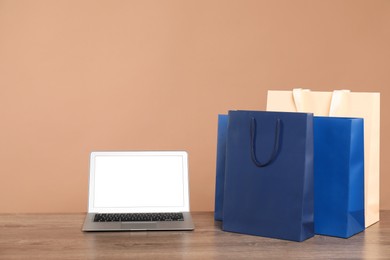 Photo of Internet shopping. Laptop and colorful paper bags on wooden table against brown background