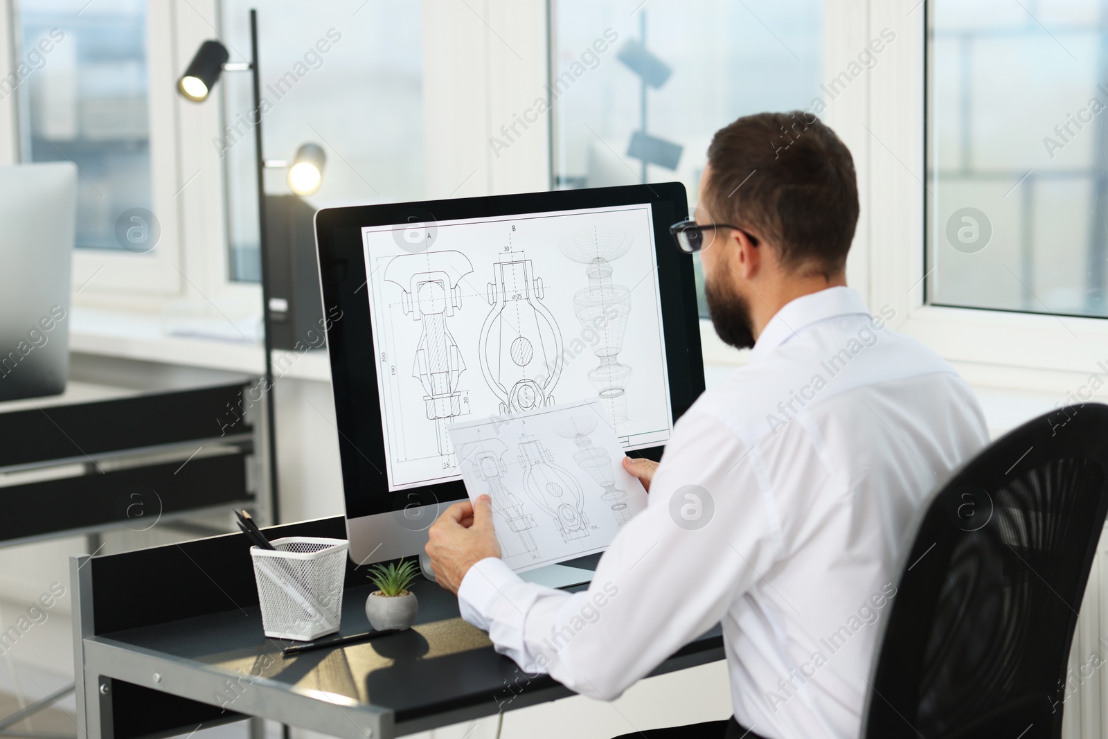 Photo of Technician making digital engineering drawing on computer at desk in office, back view