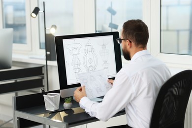 Technician making digital engineering drawing on computer at desk in office, back view