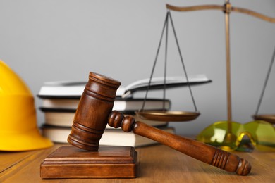 Photo of Accident at work concept. Gavel, books, scales and construction worker's protective gear on wooden table, selective focus