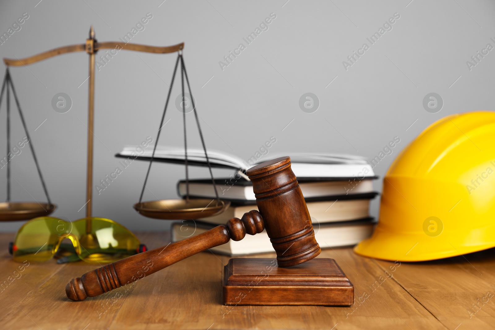 Photo of Accident at work concept. Gavel, books, scales and construction worker's protective gear on wooden table, selective focus