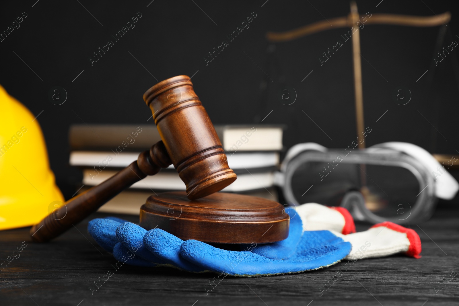 Photo of Accident at work concept. Gavel, books, scales and construction worker's protective gear on black wooden table, selective focus