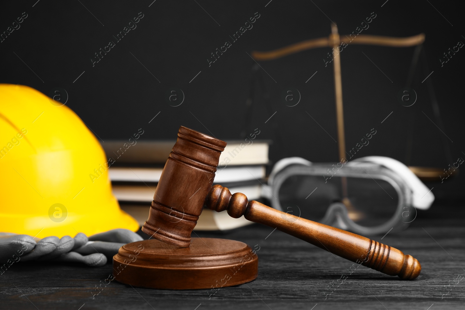 Photo of Accident at work concept. Gavel, books, scales and construction worker's protective gear on black wooden table, selective focus