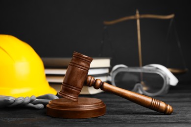 Photo of Accident at work concept. Gavel, books, scales and construction worker's protective gear on black wooden table, selective focus