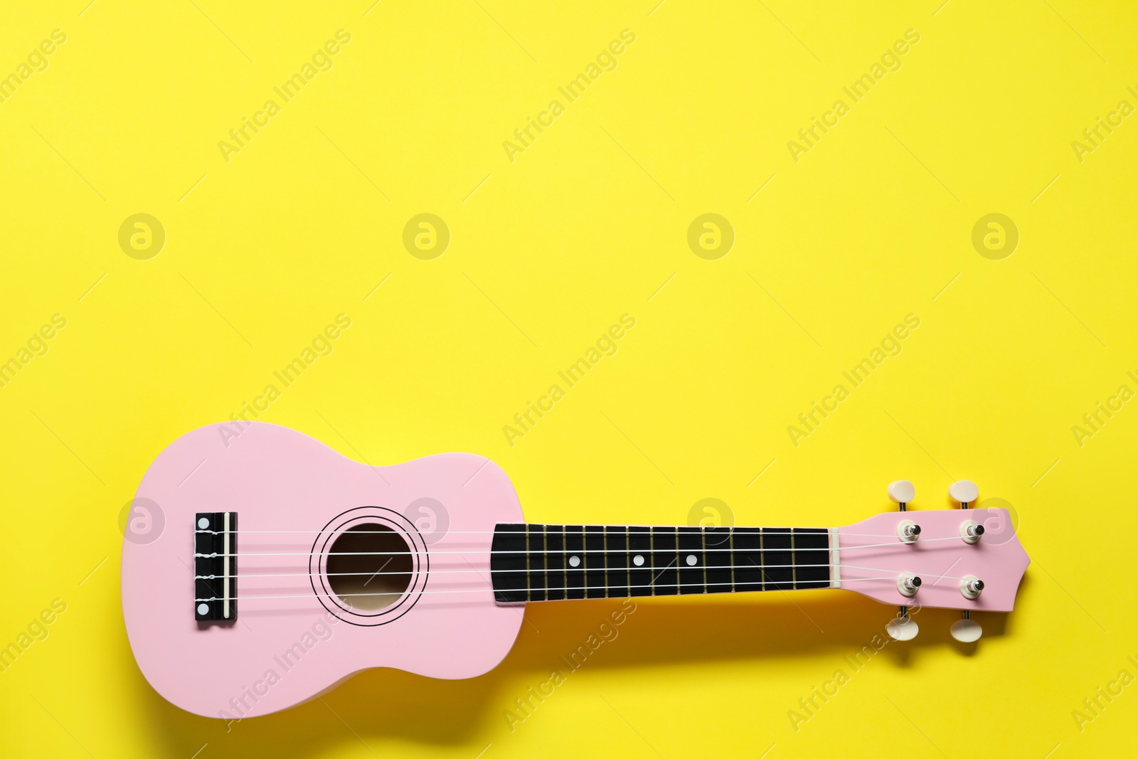 Photo of One ukulele on yellow background, top view. Space for text