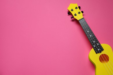 Photo of One ukulele on pink background, top view. Space for text