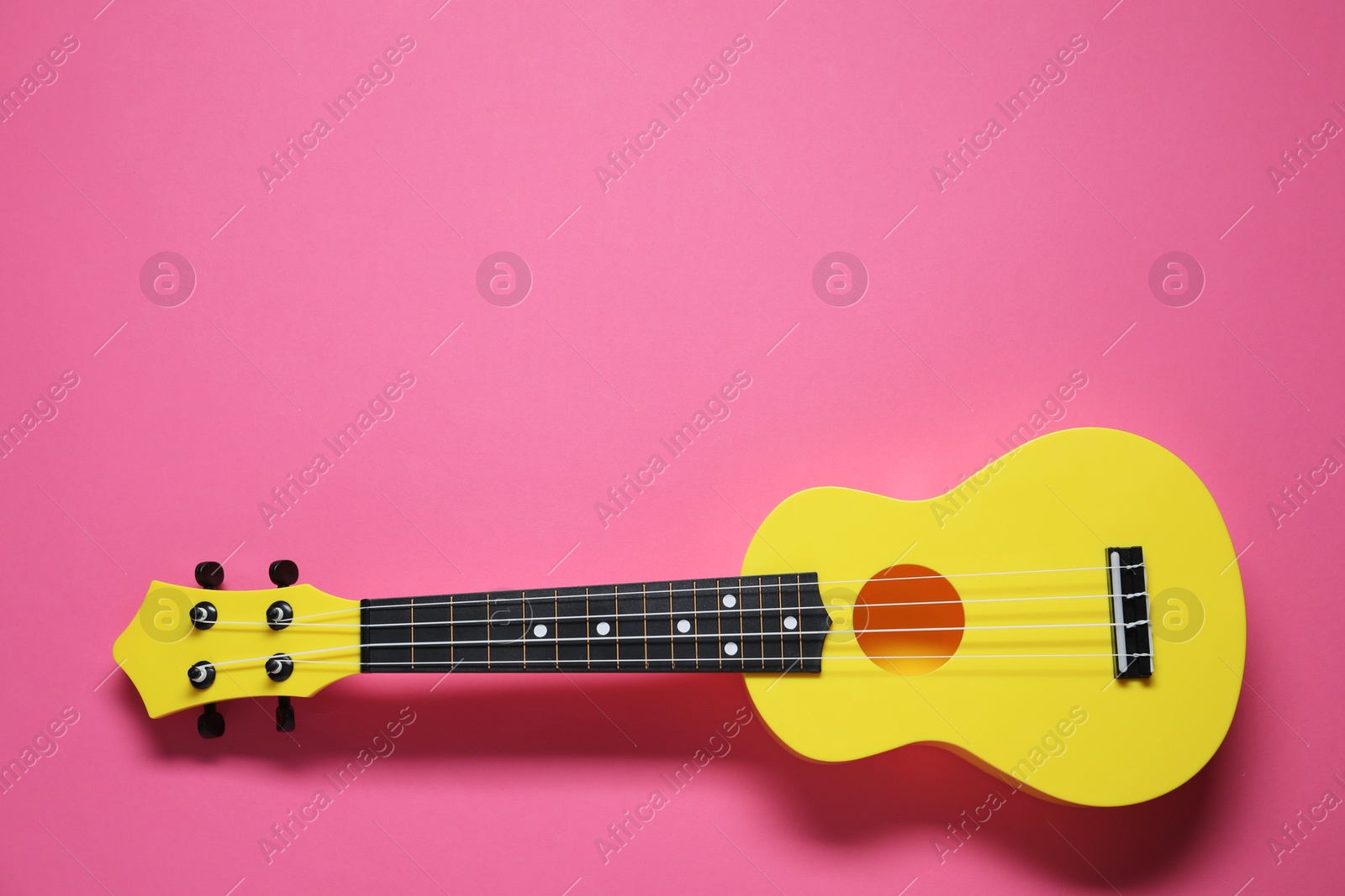 Photo of One ukulele on pink background, top view. Space for text