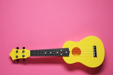 Photo of One ukulele on pink background, top view. Space for text