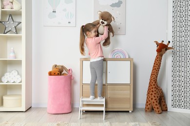 Photo of Little girl standing on step stool and playing with toys indoors